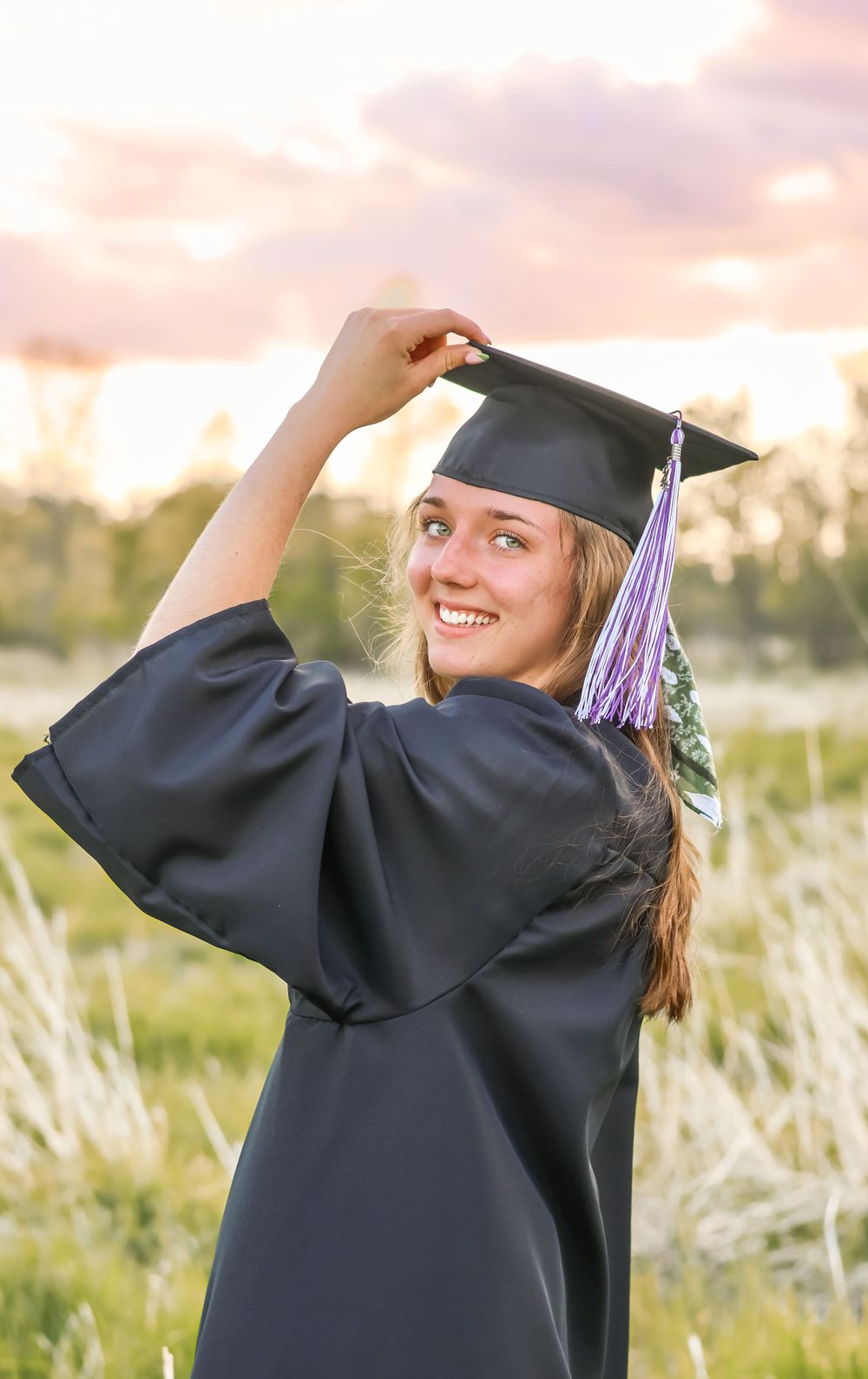 Graduate in cap and gown poses during golden hour sunset celebration.