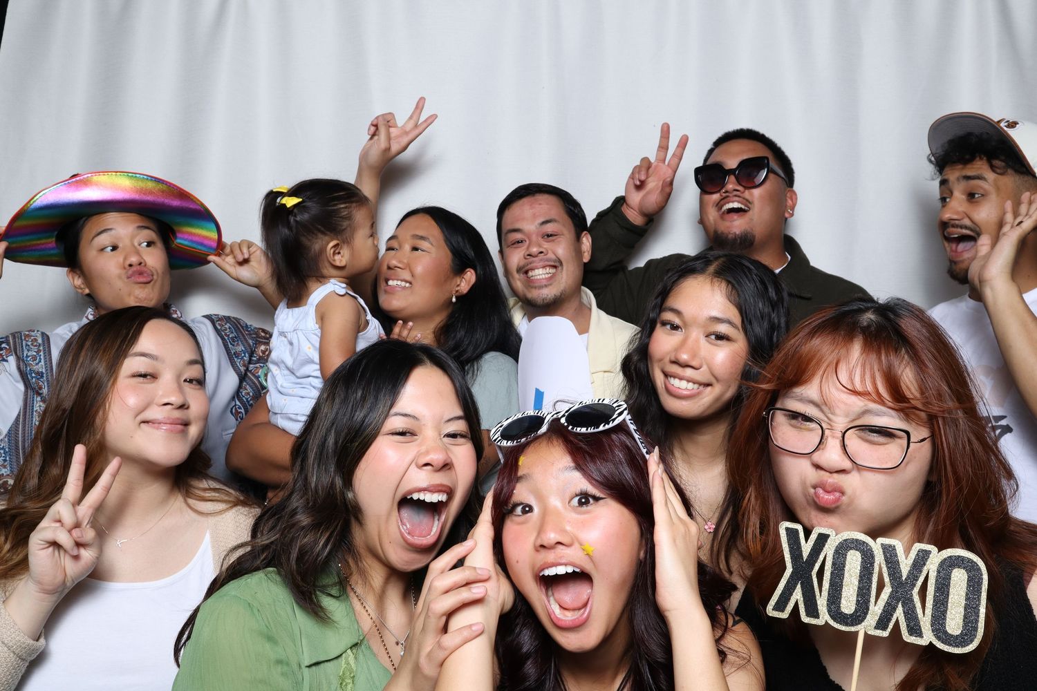 Group of six friends pose with fun props at a wedding photobooth, laughing and making gestures in the Bay Area.
