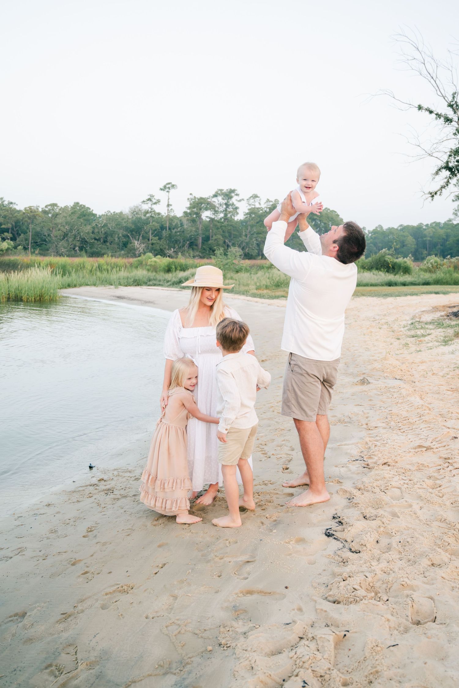 A family enjoys a peaceful moment together on a sandy beach shore next to marsh waters during sunrise.