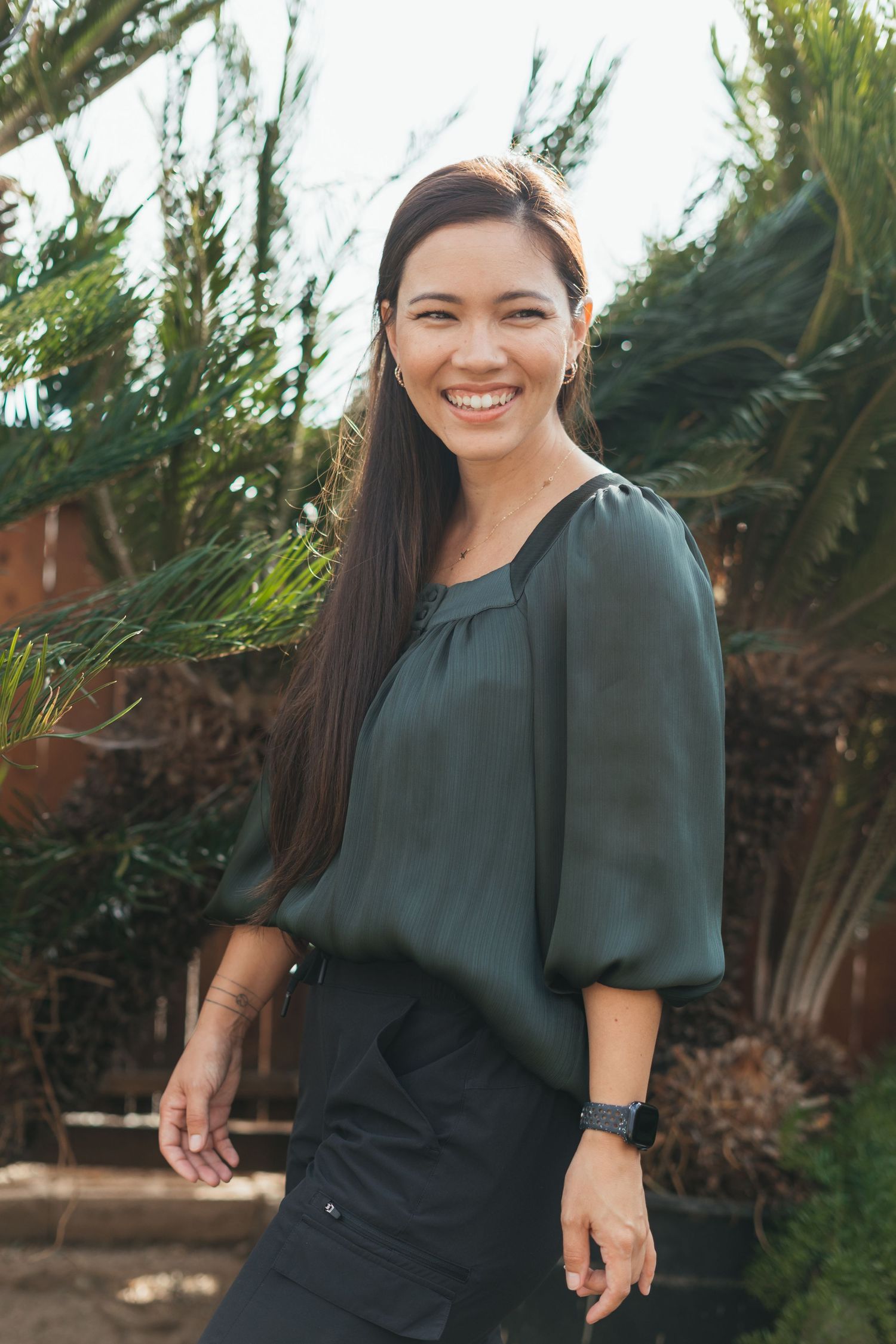 Woman in dark green blouse poses and laughs in outdoor garden setting.