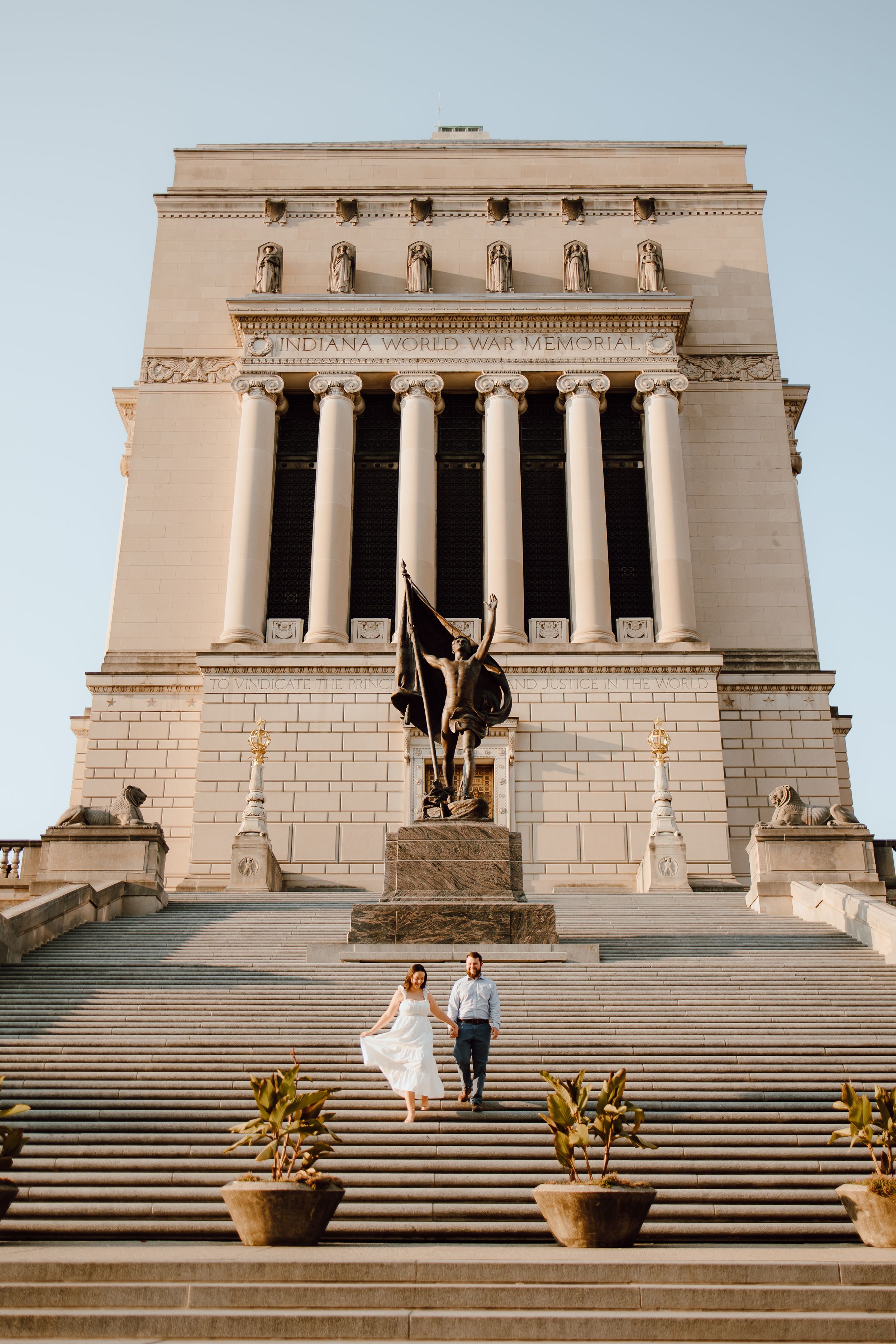 A couple stands on the grand steps of the Indiana War Memorial building with its neoclassical columns and architectural details.