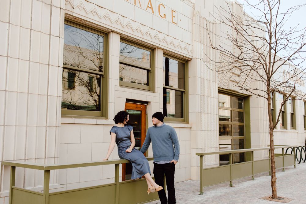 Two people stand outside a vintage storefront with white stone walls and large windows in an urban setting.