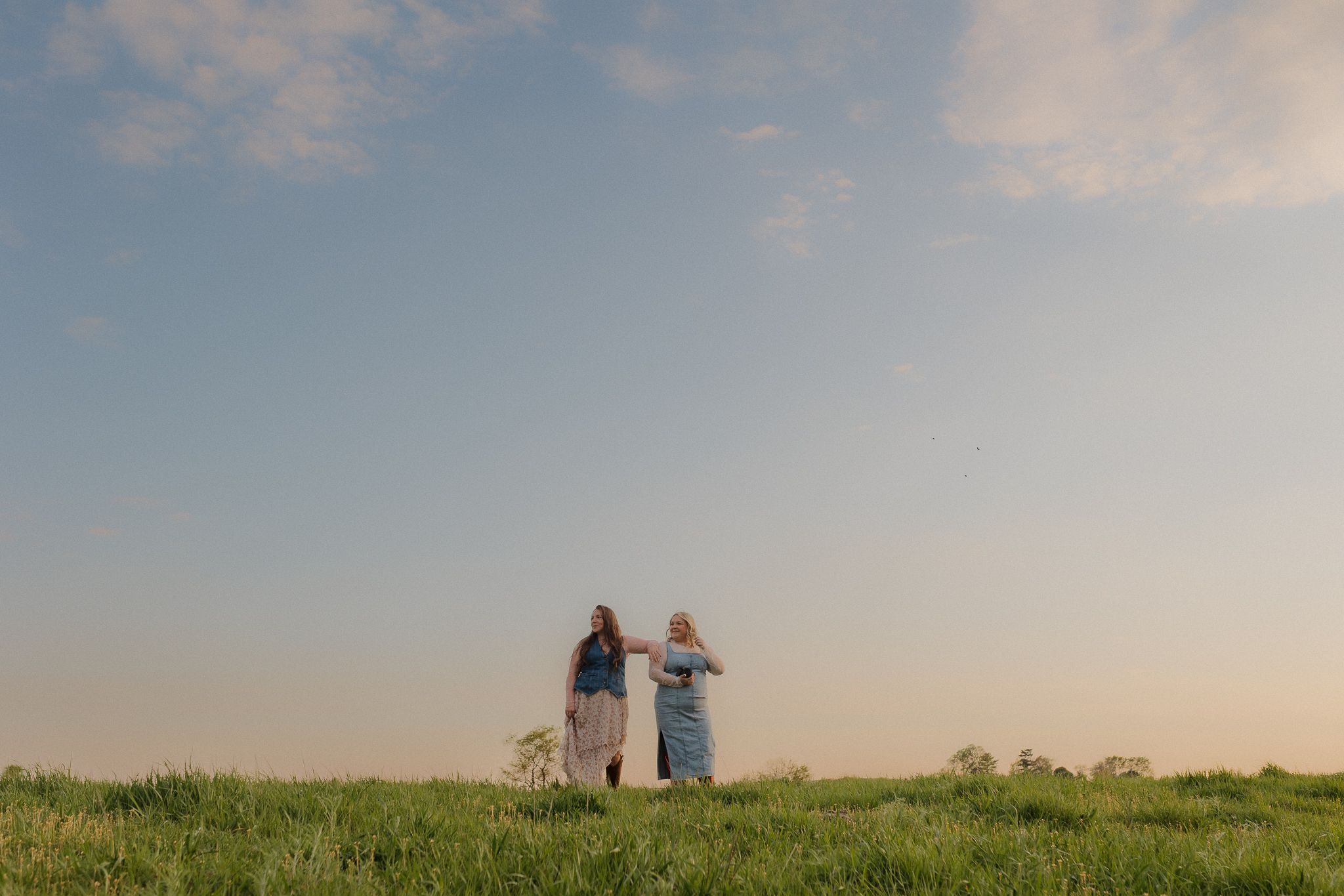 Silhouetted figures stand on a grassy hill against a soft sunset sky during golden hour.