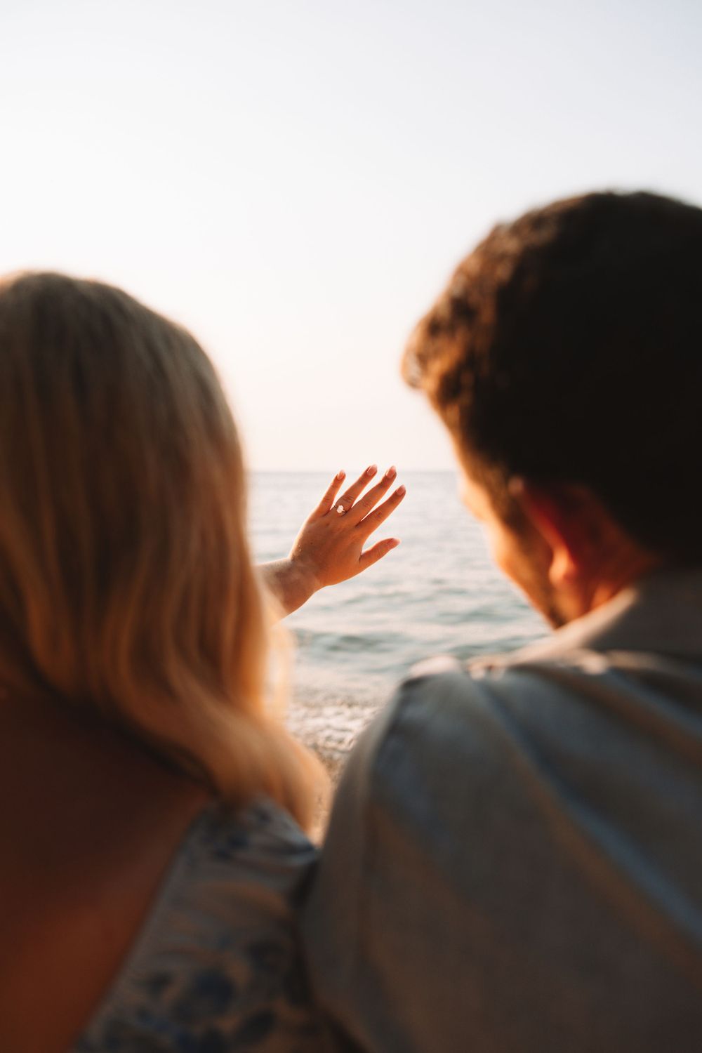 Couple at the beach watching the sunset and admiring ring on hand—Traverse City engagement photography.