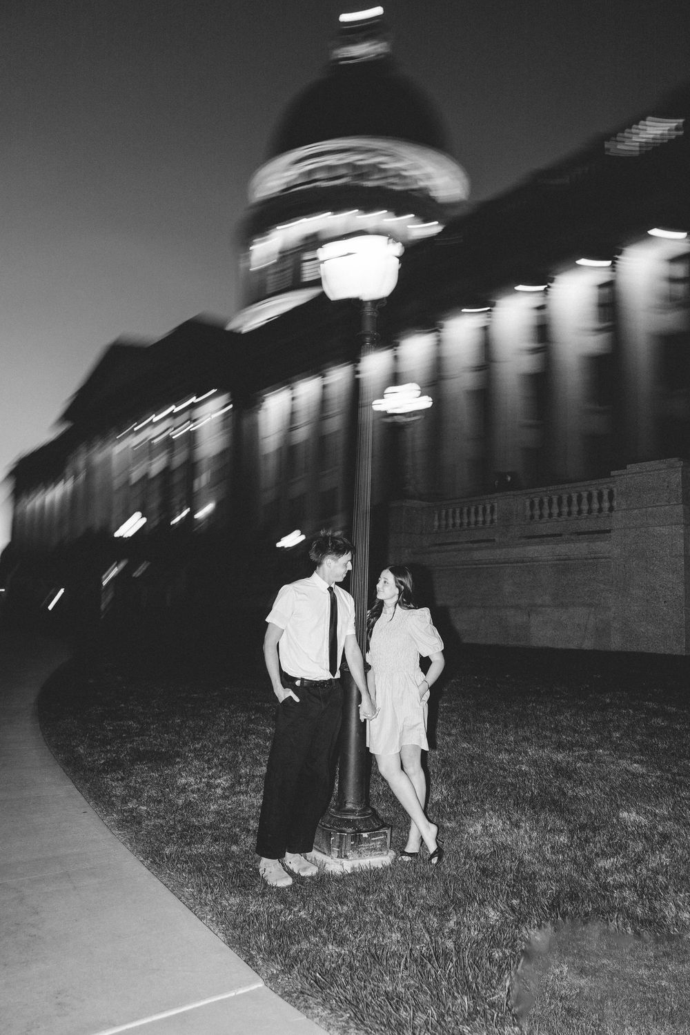 Couple posing for couples photoshoot at the Utah State Capitol Building at night dancing around a light pole.