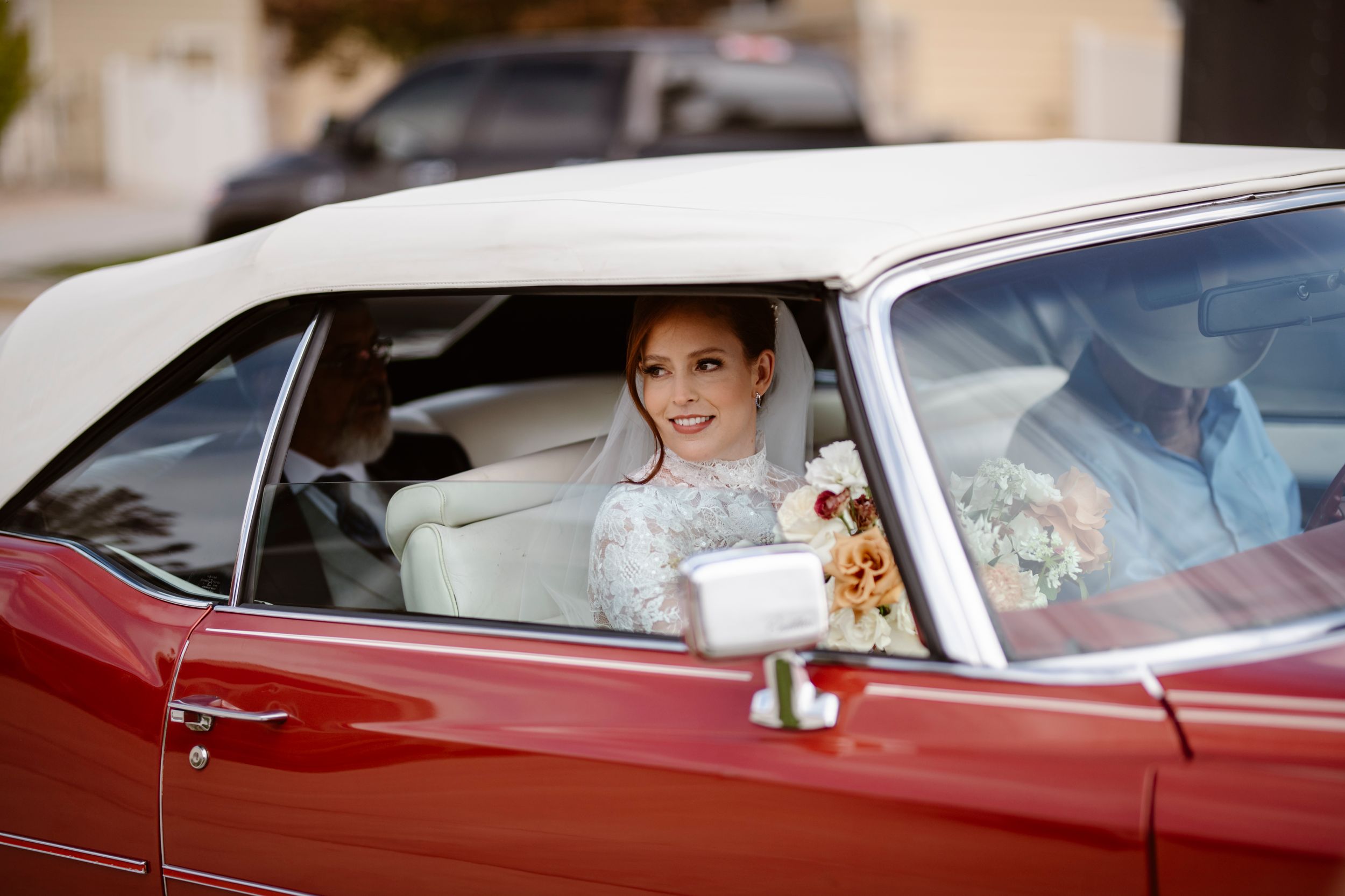 Classic red and white vintage car with bridal passenger visible through window.