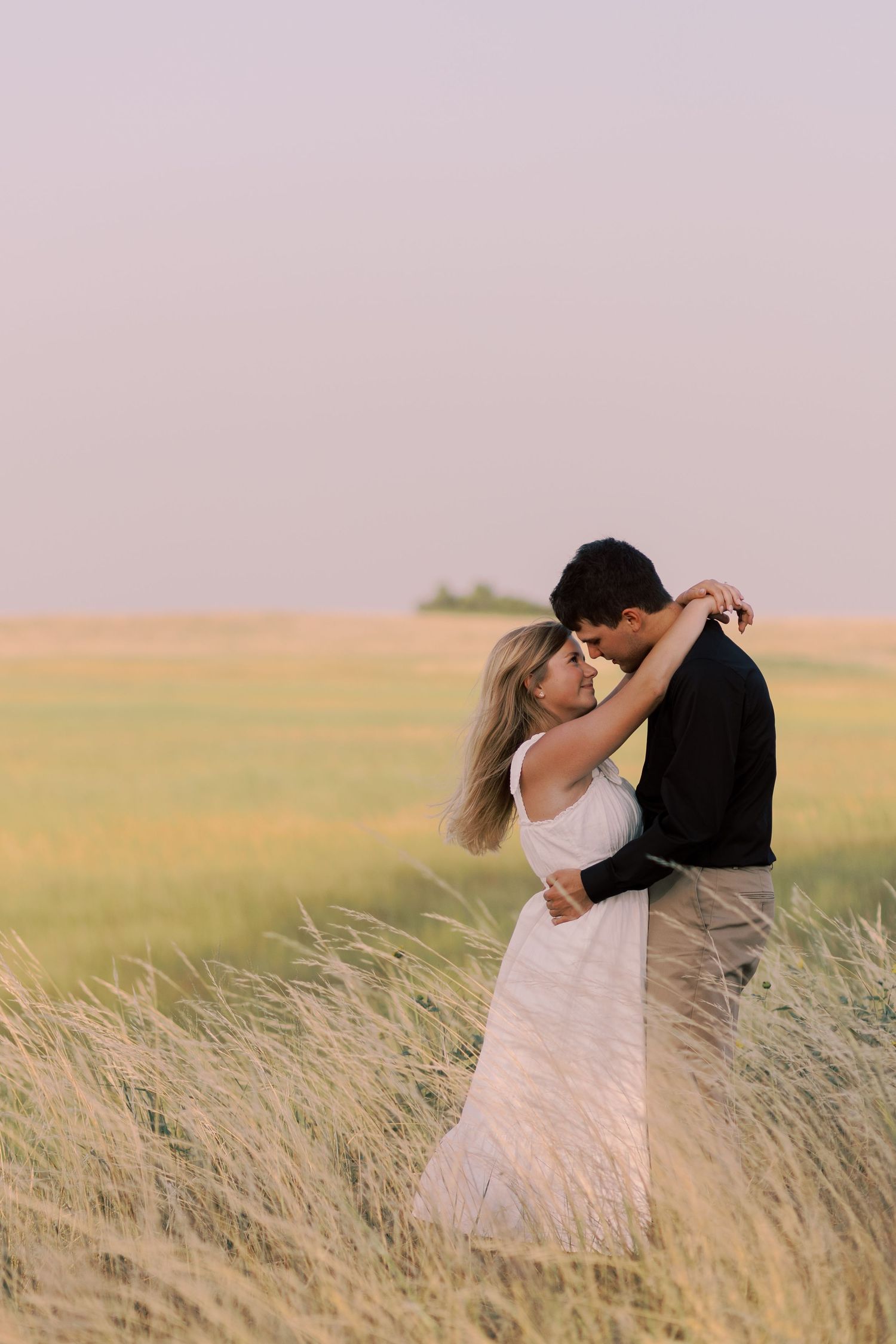 A couple sharing an intimate moment while standing in a golden wheat field at sunset.
