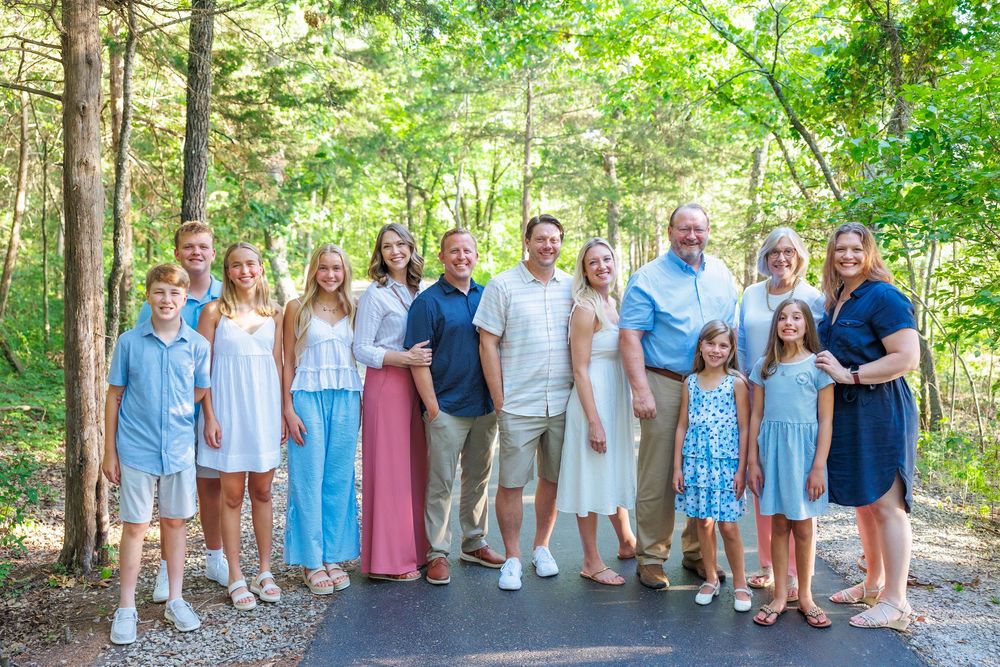 A large family group wearing coordinated blue and white outfits poses together for outdoor photos in a wooded setting.