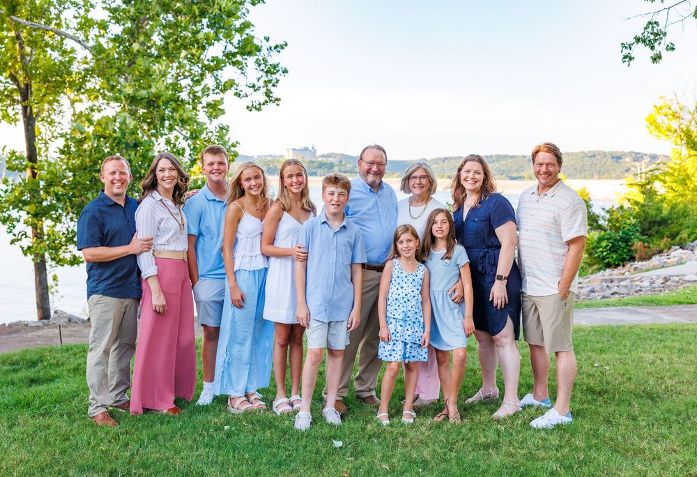 A group of people in coordinated blue and pink outfits pose together outdoors on a sunny summer day.