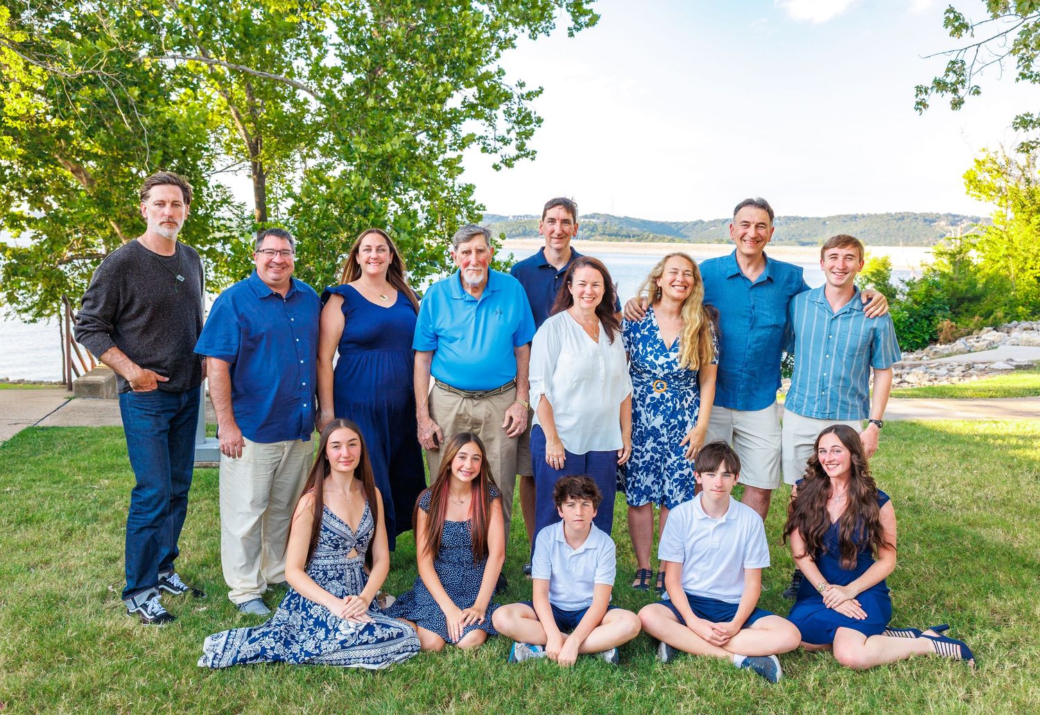 A group of people wearing blue and white clothing pose together outdoors on a grassy area during a sunny day.