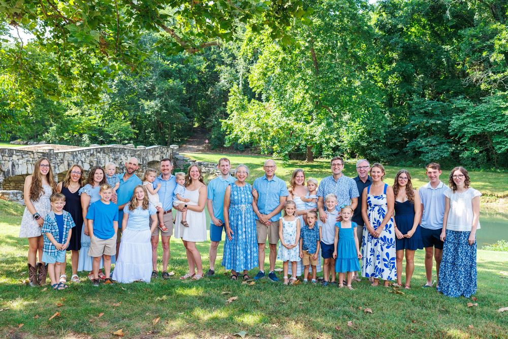 A group of people in coordinating blue and white outfits pose together outdoors in a park setting.