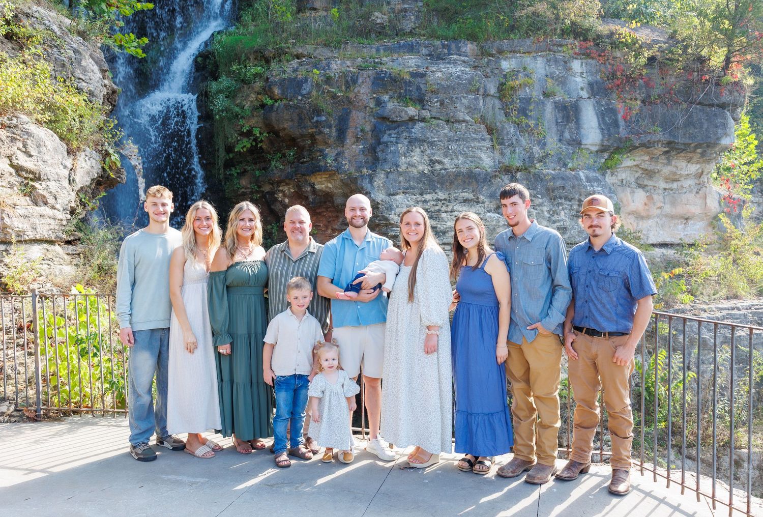 Family group portrait session at scenic waterfall location wearing coordinated blue and neutral colored outfits.