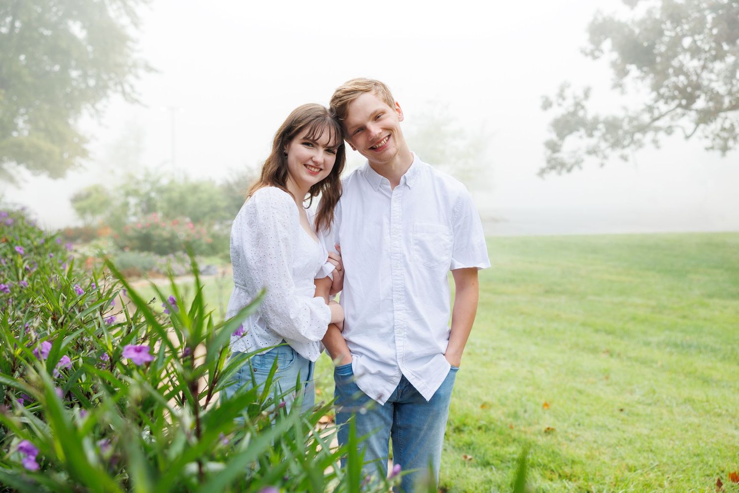 A couple shares a romantic moment together in a misty green field during an engagement photo session.