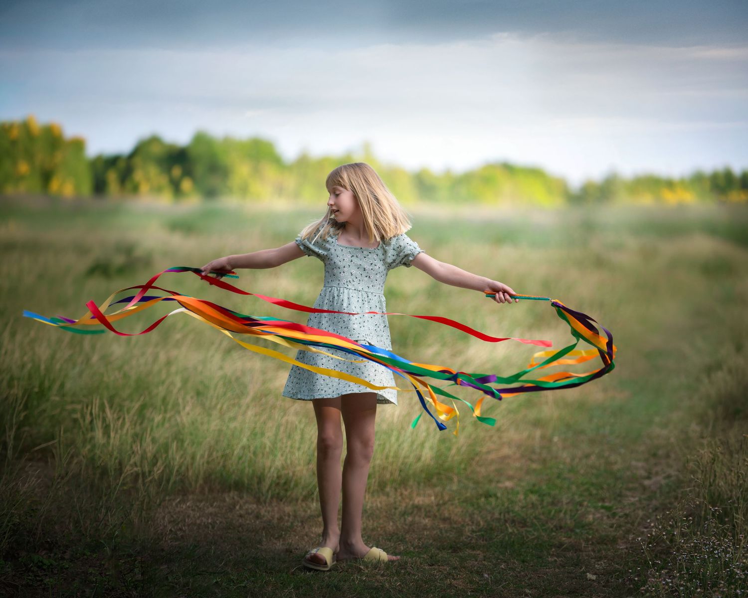 A barefoot girl in a floral dress twirls colorful ribbons in an open field.