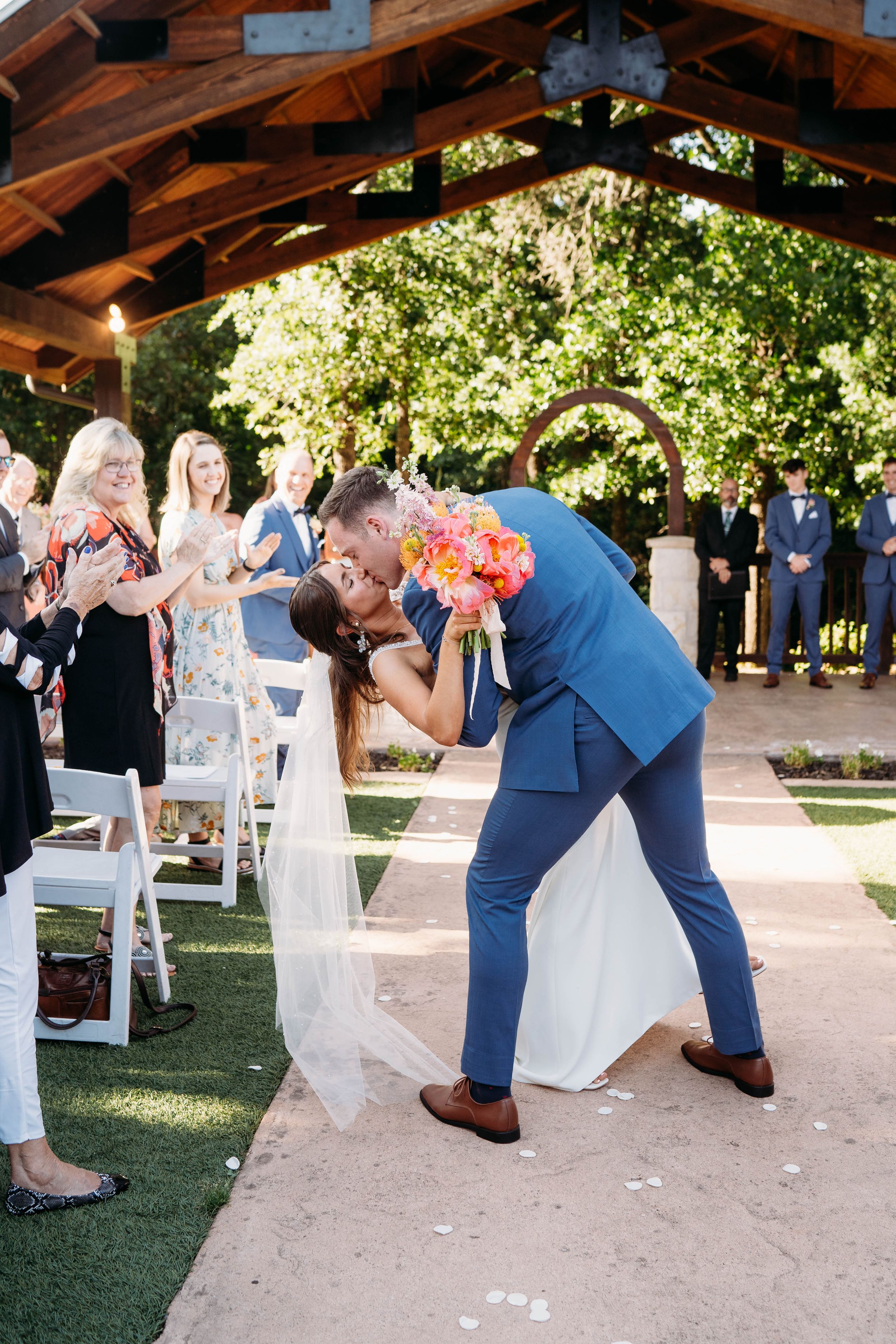 A romantic moment during an outdoor Oklahoma wedding ceremony under a wooden pergola.