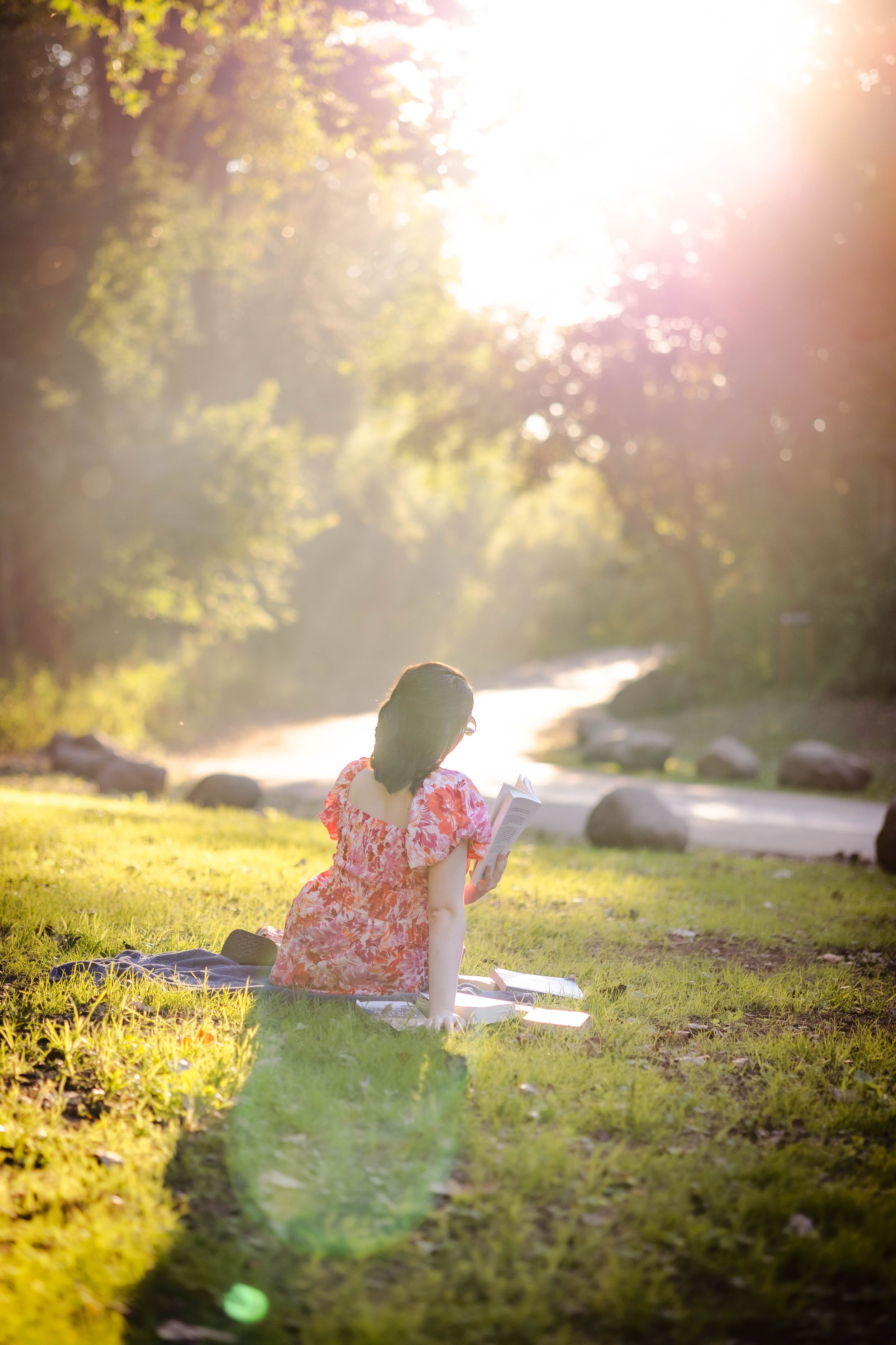 Person in floral dress sits in golden sunlit meadow.