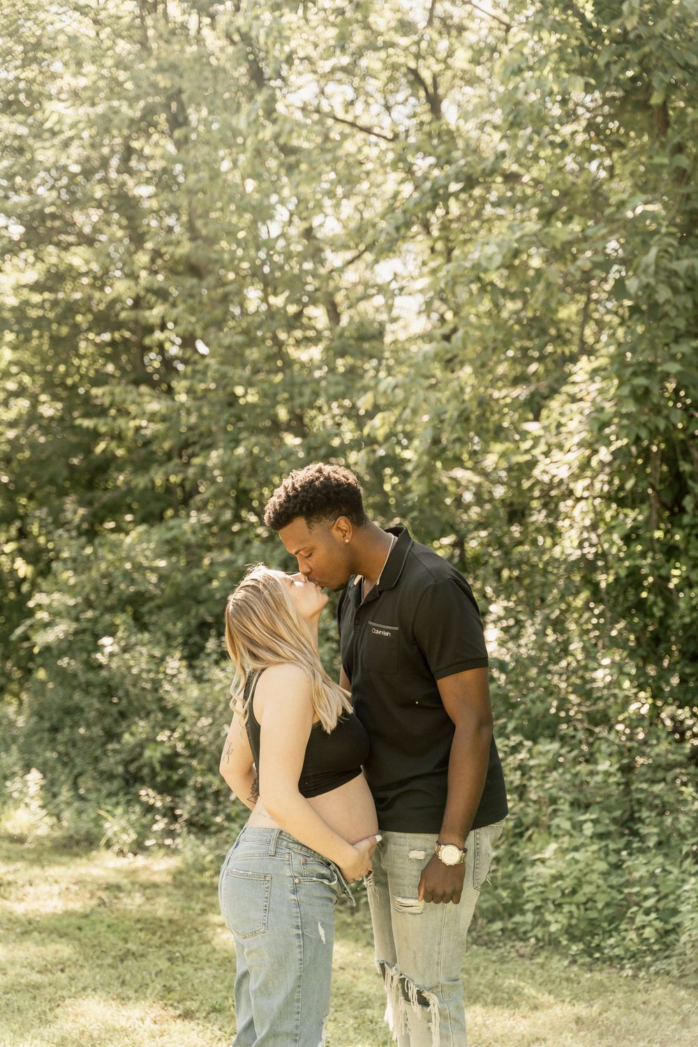 Romantic couple sharing tender moments in a sunlit garden setting with green foliage backdrop.