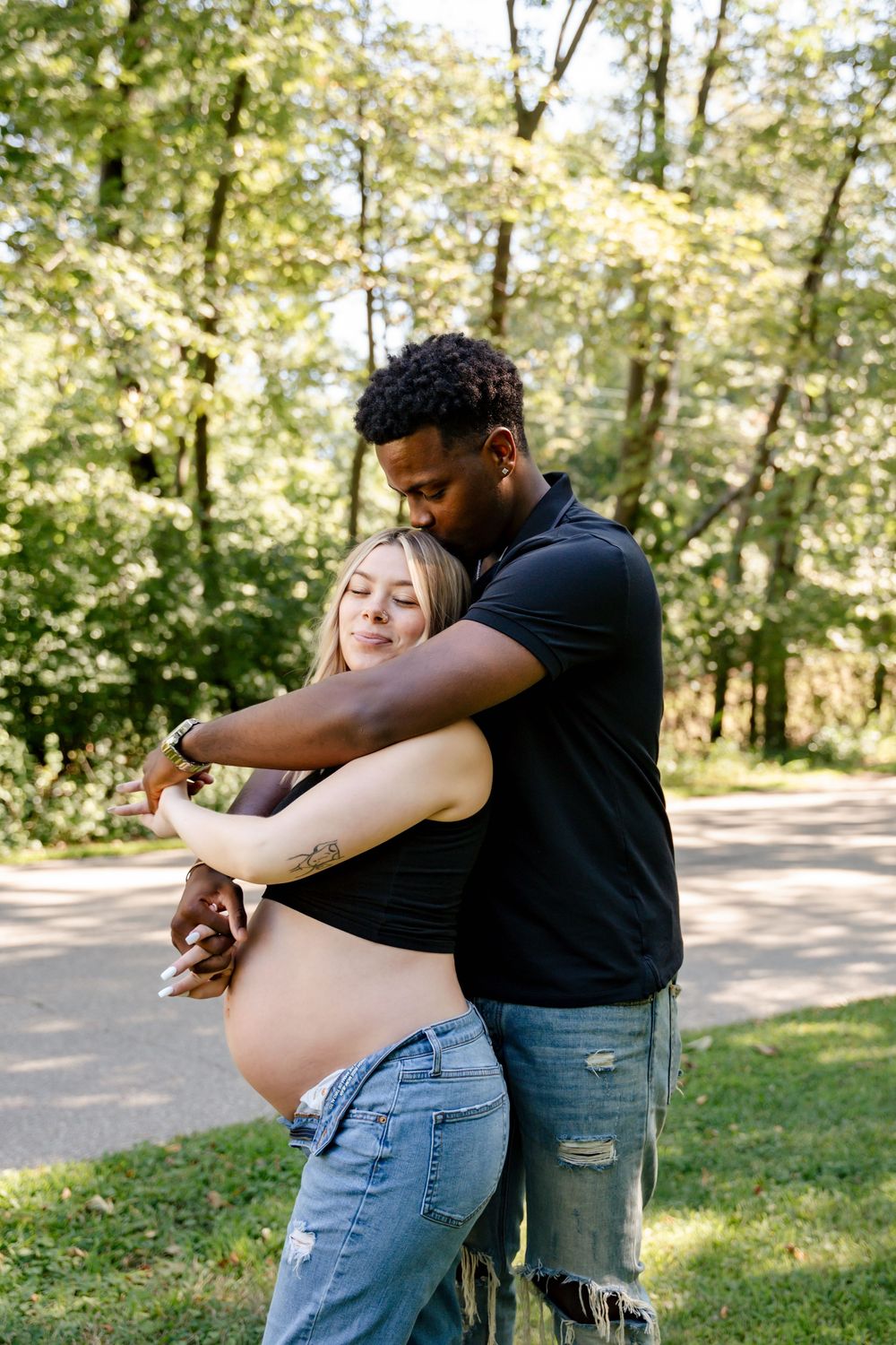A couple embraces tenderly in a sunlit forest setting, creating an intimate outdoor moment.
