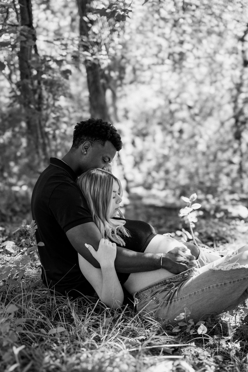 A couple relaxes together on the grass in a dreamy black and white forest setting.
