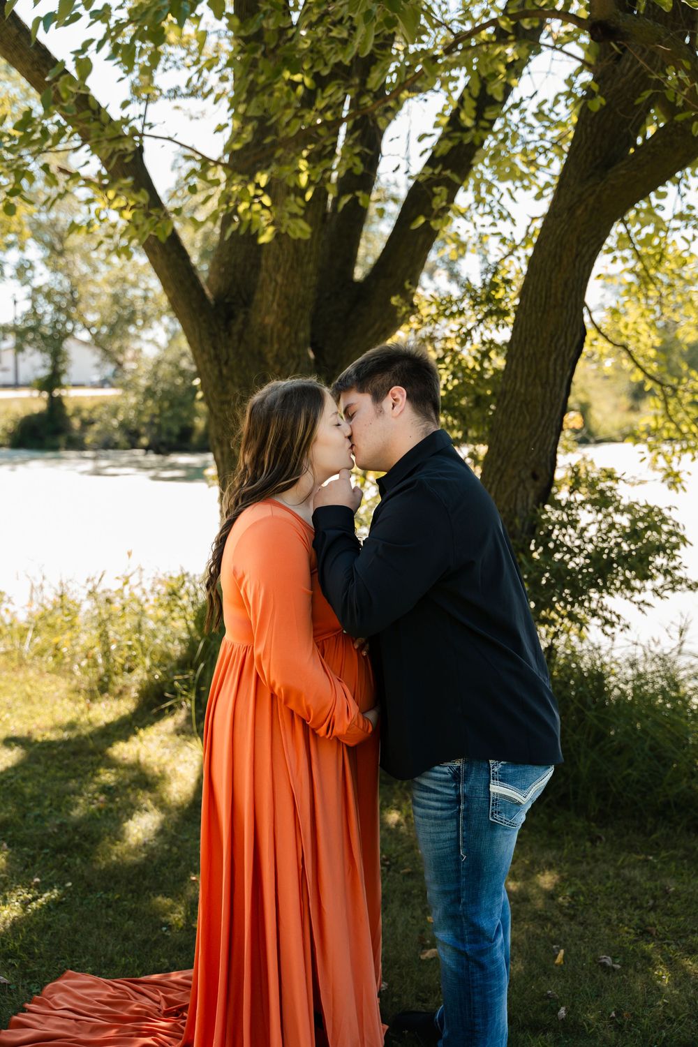 A couple embraces under autumn trees with sunlight filtering through the branches.
