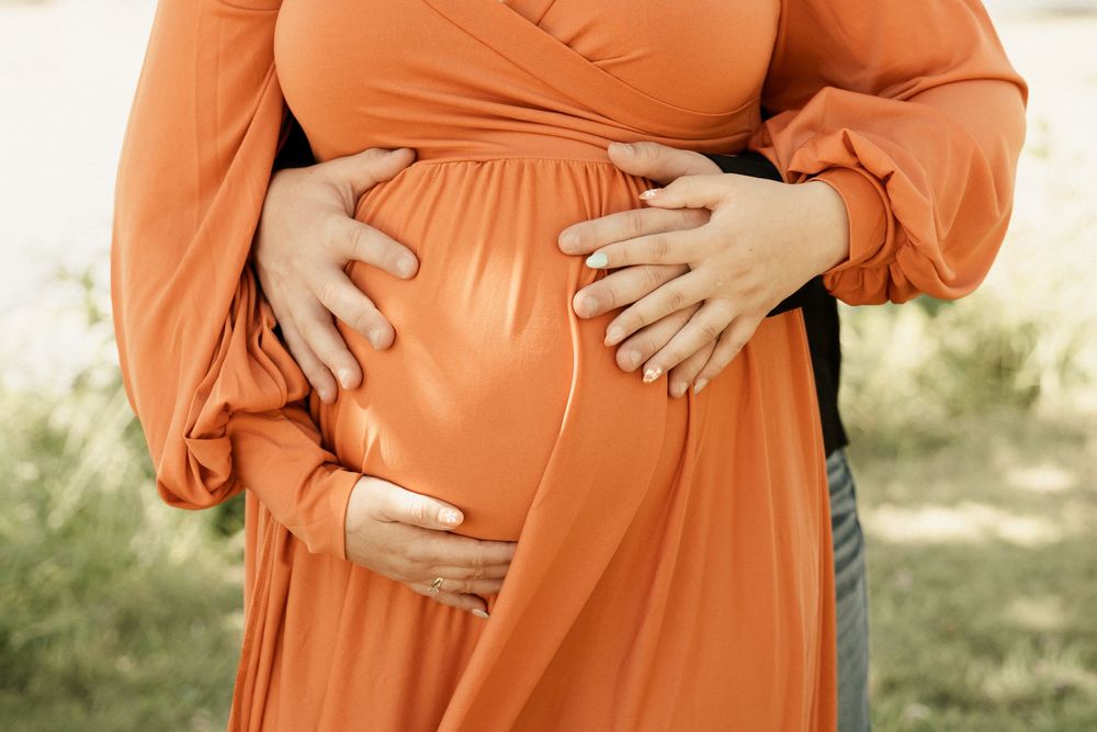 Close-up of hands tenderly placed on a vibrant orange maternity dress.