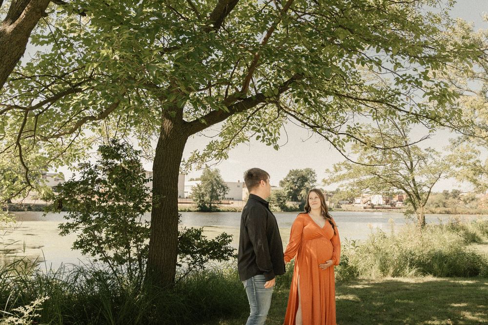 A scenic maternity photo session under trees with golden sunlight filtering through.