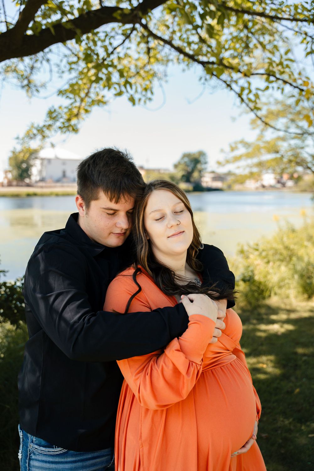 A couple shares an intimate embrace while looking at their phones in a sunlit outdoor setting.