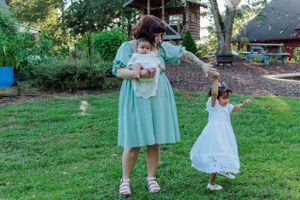 A heartwarming scene in a garden with a baby and young child in a white dress.
