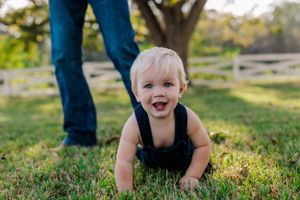 A toddler in overalls crawls happily through green grass during golden hour.