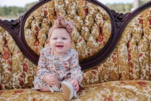 Baby sitting on vintage floral couch with ornate wooden frame.