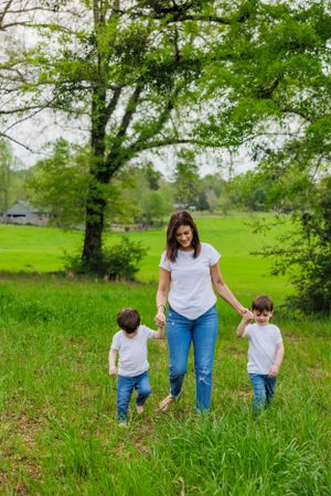 Family walking hand in hand through a verdant spring meadow beneath a large tree.