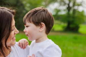 Intimate moment shared between parent and child against green outdoor backdrop.