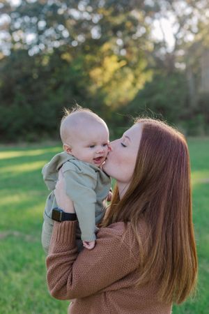 A tender maternal moment captured outdoors in a park during golden hour.
