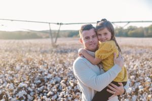 A heartwarming moment captured in a cotton field with warm sunlight filtering through the scenery.