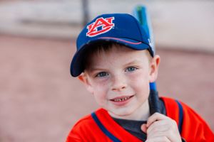 A young sports fan wearing an Auburn baseball cap and orange shirt smiles at the camera.