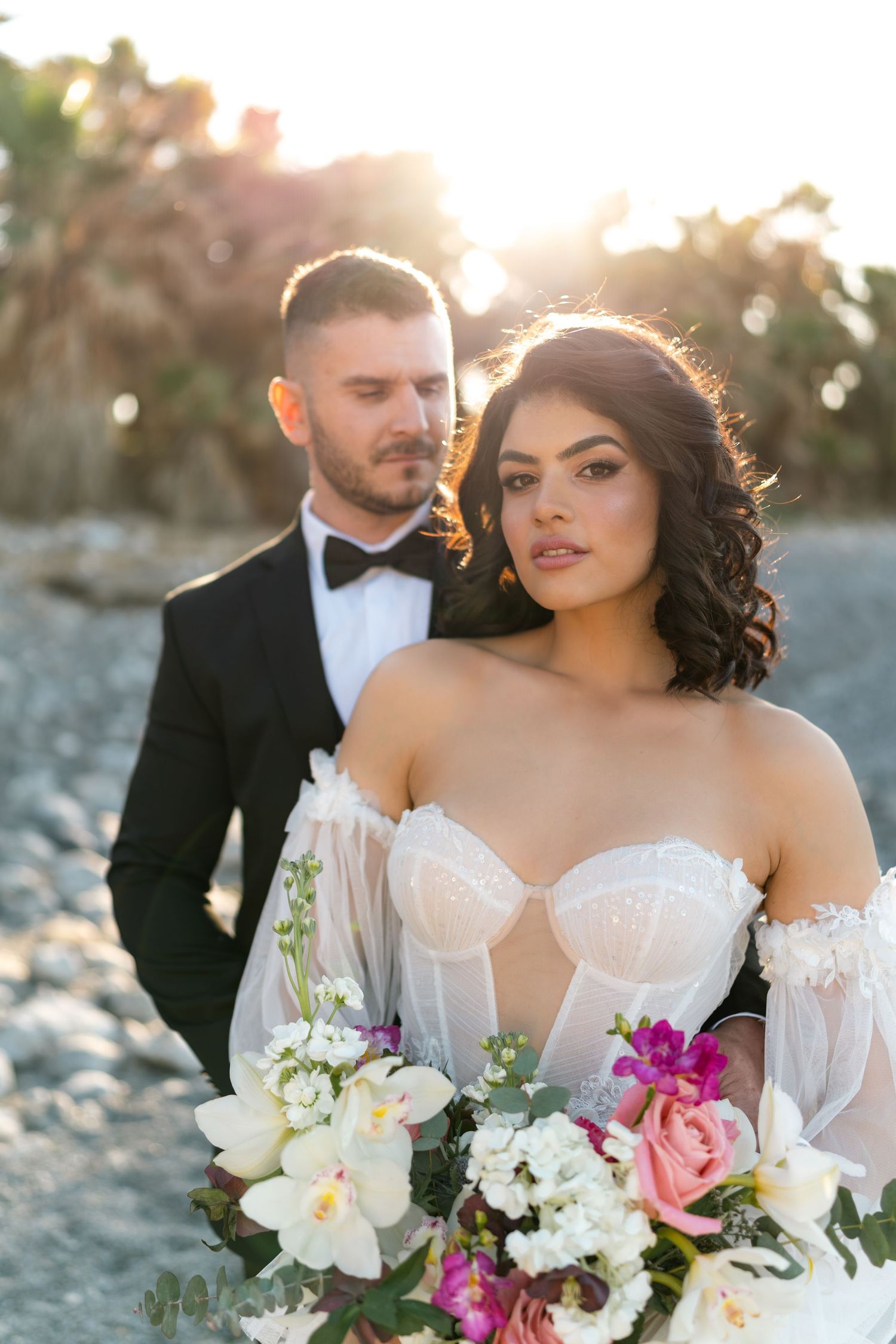 Romantic sunset wedding portrait with a colorful bouquet on a beach.