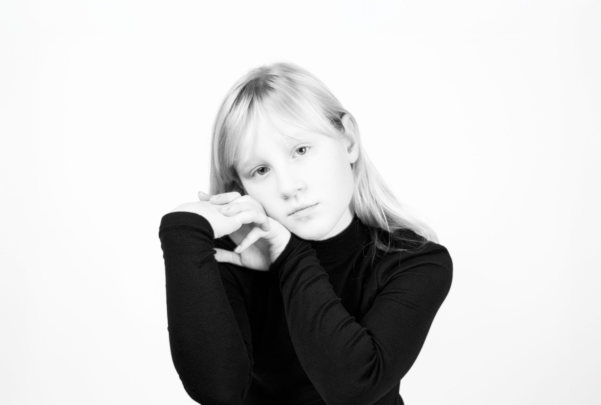 Black and white portrait of a young blonde girl in a black turtleneck, resting her chin on her hands.