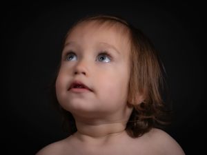 A child with light brown hair looks upward against a dark background in dramatic lighting.