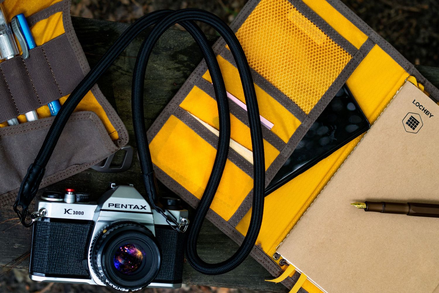 Vintage Pentax camera with strap laid next to yellow notebook and pencil.