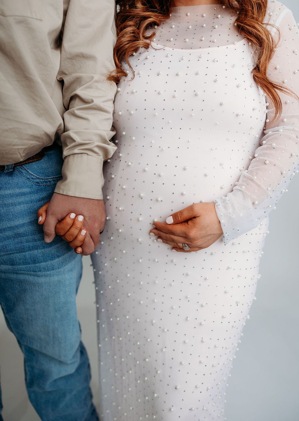 Couple holding hands with woman wearing elegant white beaded long sleeve dress and man in casual jeans and sweater.