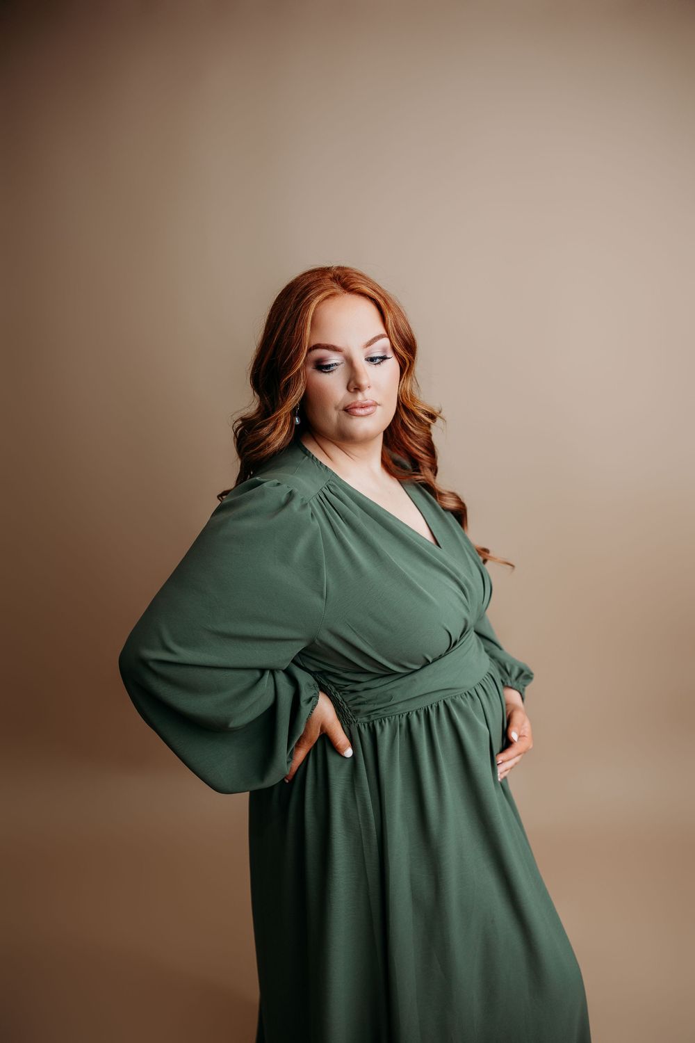 A figure in a flowing emerald green dress poses elegantly against a neutral beige backdrop.