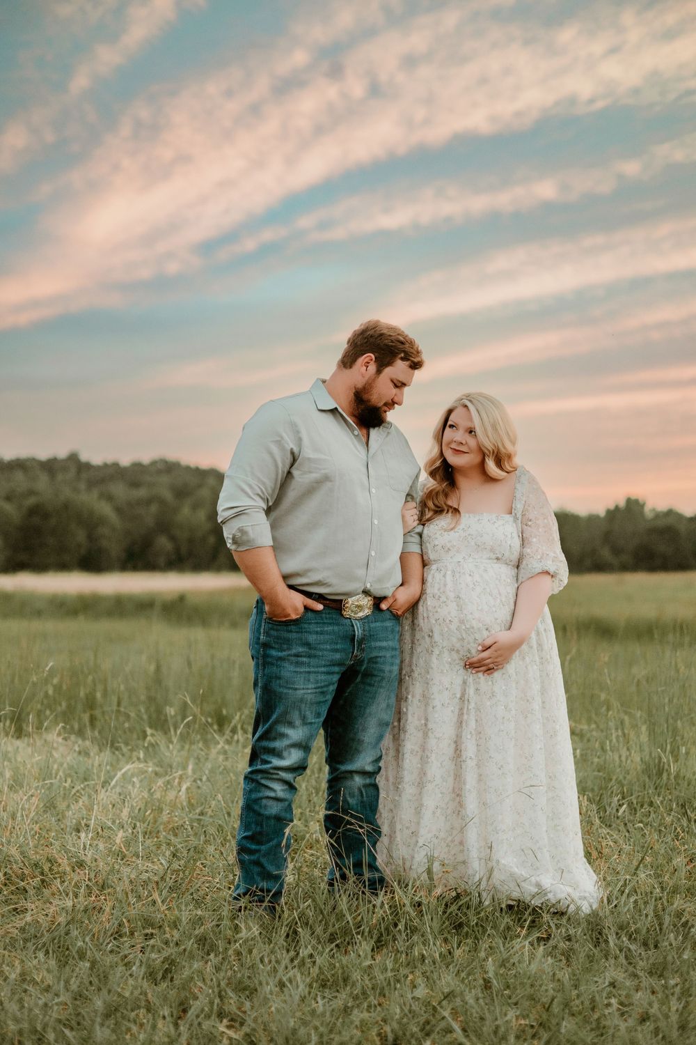 Couple poses in meadow during golden hour for romantic maternity photography session.