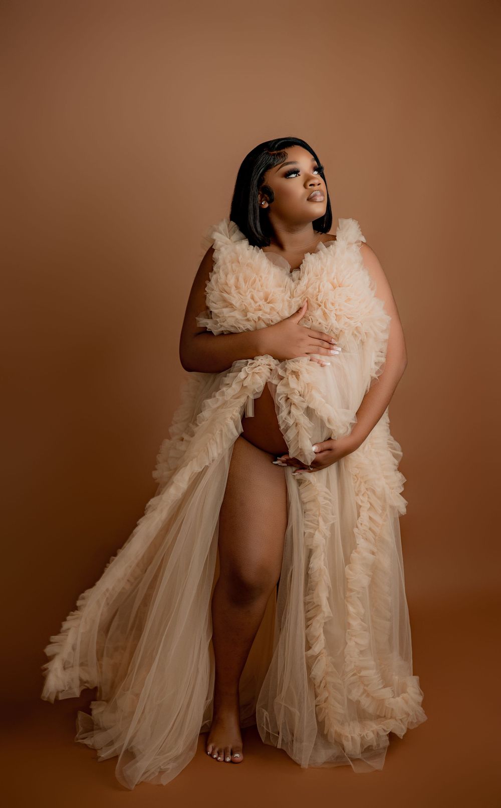 Romantic maternity portrait in flowing peach tulle gown against brown background.
