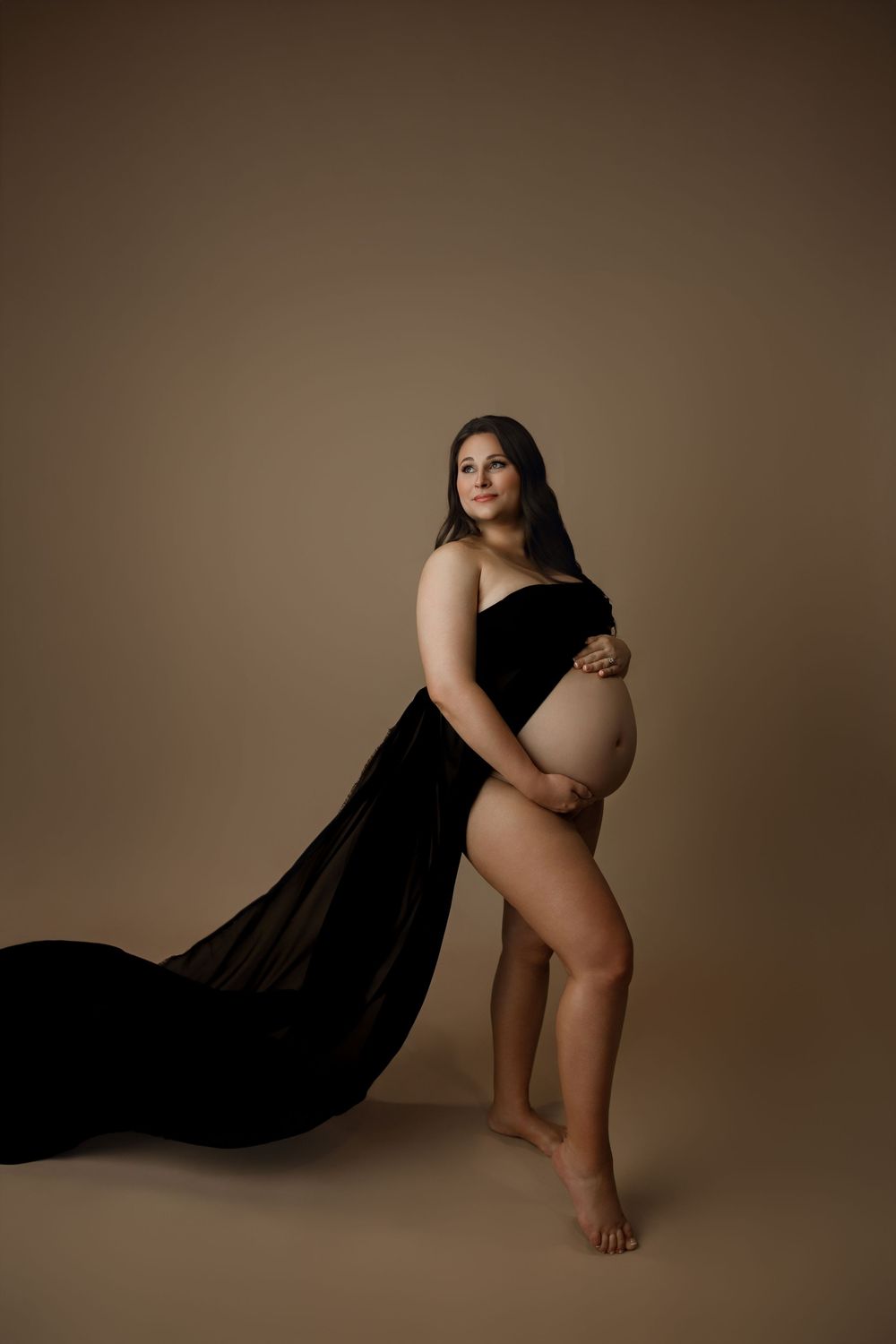 Artistic maternity silhouette series against warm brown backdrop showing graceful poses and flowing black fabric.