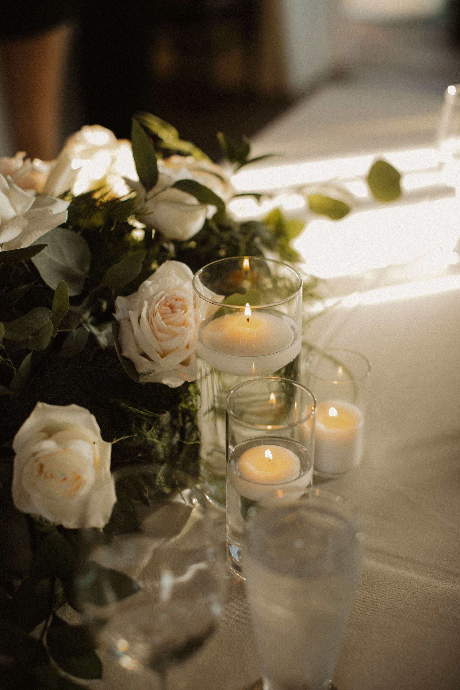 Elegant table decor featuring white roses and glowing candles in glass holders.