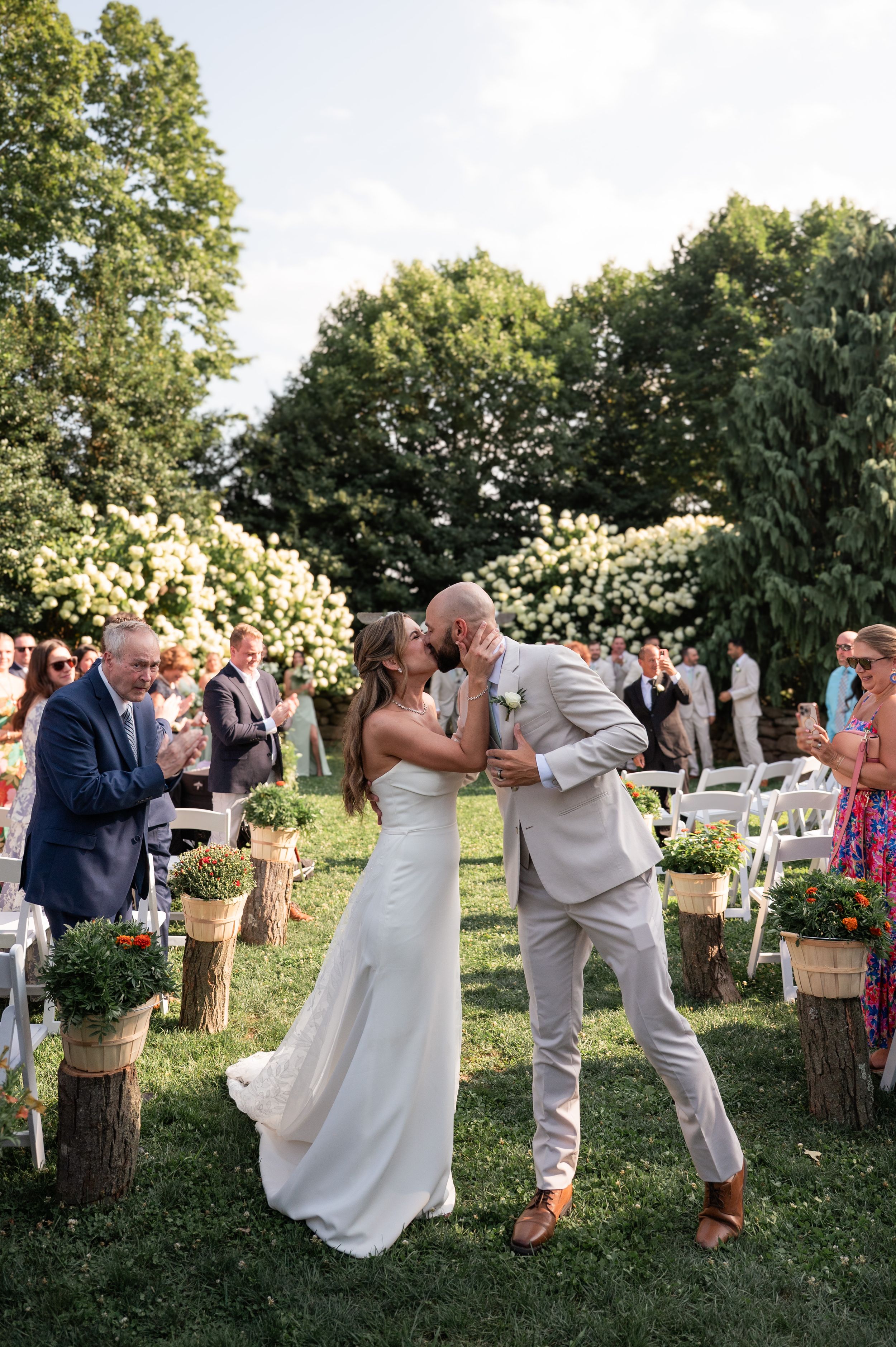Wedding celebration in a garden setting with guests and white flower decorations.