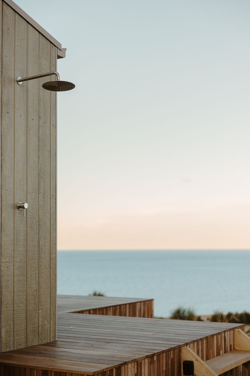 Outdoor shower stalls with wooden siding overlooking ocean horizon.