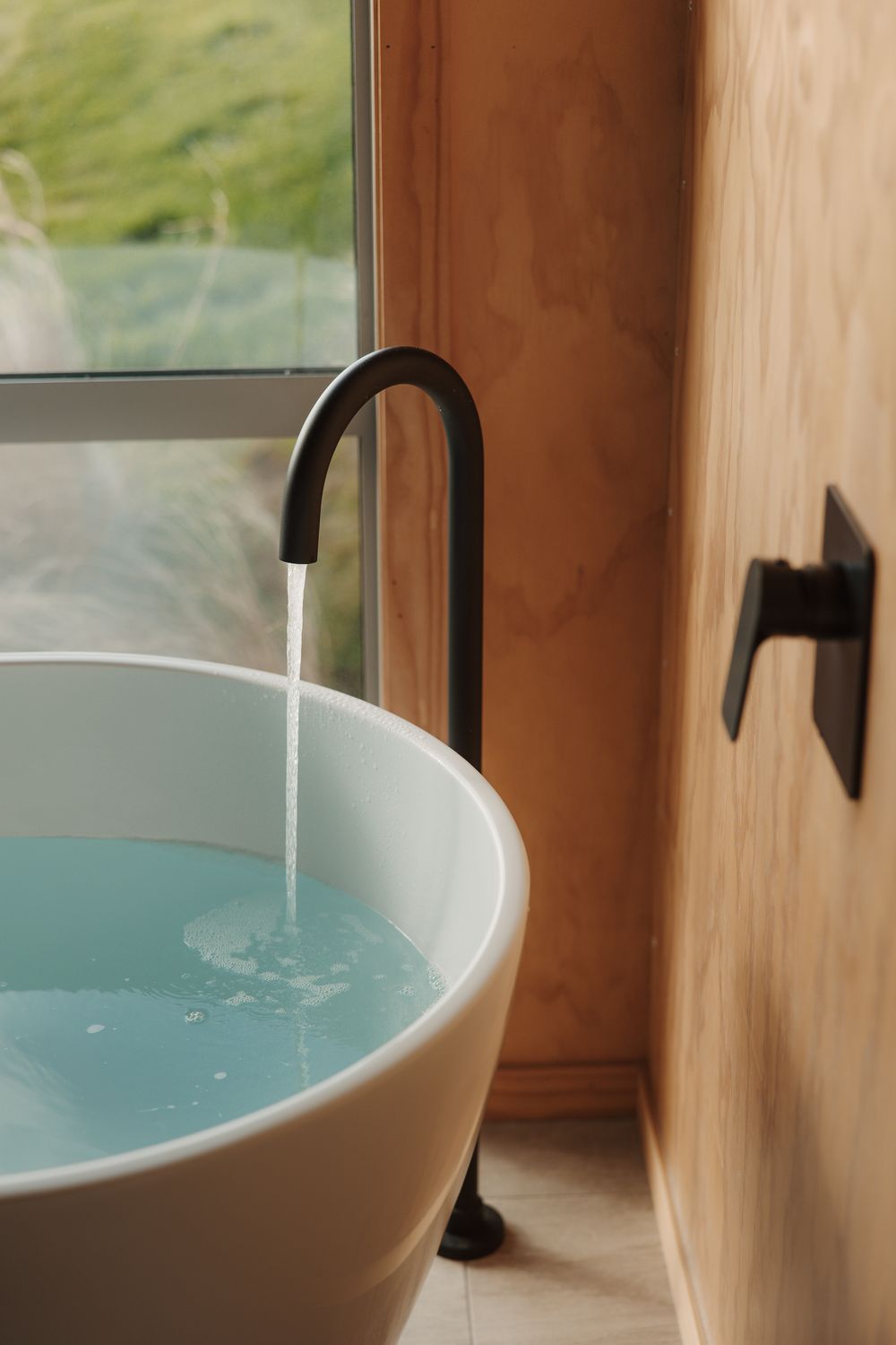 Modern white freestanding bathtub with matte black faucet near a window with scenic views.