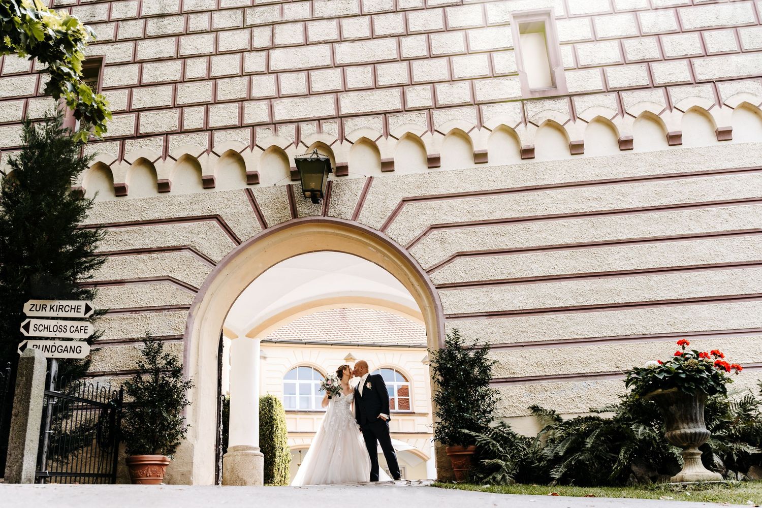 Hochzeit auf Schloss Guteneck bei Schwandorf, Brautpaar unter einem Torbogen vor historischer Architektur, Hochzeitsreportage in Bayern.