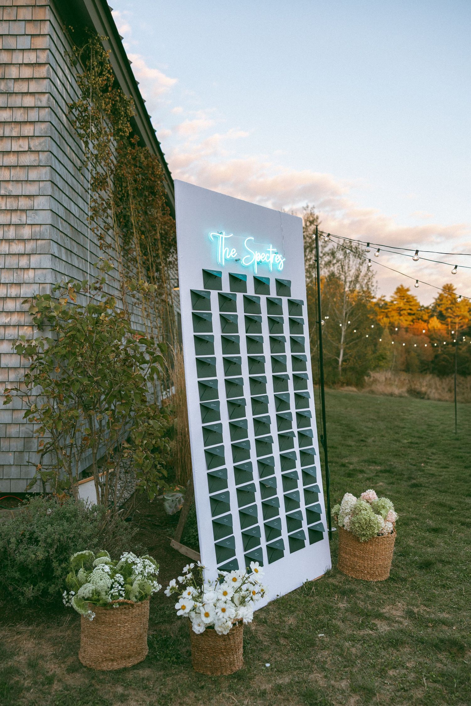 Modern seating chart display with window panes and floral baskets at outdoor wedding venue.